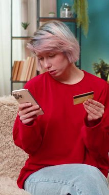 Genç bir kadın mutlu bir şekilde online alışveriş yapıyor, akıllı telefon ve kredi kartı kullanıyor, gülümsüyor, başını sallıyor. Beyaz kız e-ticaretten zevk alıyor, neşeli olumlu alıcı jesti, koltukta oturuyor.