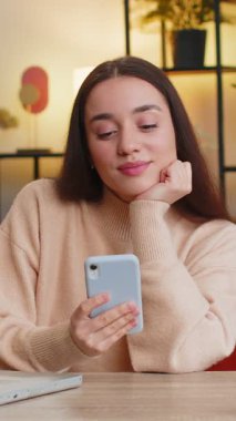 Masada oturan beyaz bir kadın ofis odasındaki dairede cep telefonu tebessümleri kullanıyor. Akıllı telefon sosyal medya uygulamaları üzerinden rahatlama filmi izlerken mesajları paylaşan bir kız.