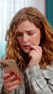 Evde endişeli bir şekilde önemli bir mesaj bekliyor. Akıllı telefonu kaydırırken tırnağını yiyor. Kanepede oturan beyaz saçlı kız gergin, stresli, duygusal beklenti, gerilim anı