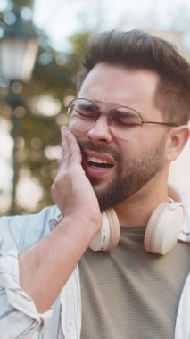 Açık havada duran beyaz bir adamın portresi diş ağrısı kötü kötü semptomlar hissediyor çene çenesinde el ele tutuşmaktan acı çekiyor diş sinirlerine zarar vermek tıbbi yardıma ihtiyaç duyuyor. Şehir sokağındaki adam.