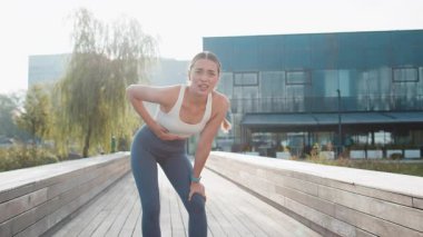 Güneşli bir günde şehir parkında koşarken karın ağrısı çeken beyaz bir koşucu. Üzgün kadın elini karnının üstünde tutuyor. Kızda zehirlenme, kabızlık, spazm ya da adet görme var..