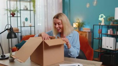 Bavulları açan mutlu sarışın iş kadını dairede masa başında oturuyor. Gülümseyen tatmin olmuş kız alışverişci internet müşterisi karton kutu açıyor hızlı posta yoluyla satın alma hediyesi alıyor
