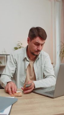 Planlama bütçesi. Zengin ve mutlu bir adam, evdeki faturaları hesaplamak için dizüstü bilgisayarla euro nakit para sayıyor. Adam gelir gelirinden, planlı tatil hediyeleri için paradan memnun. Dikey.