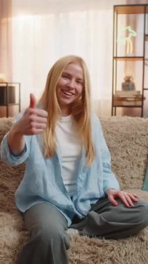 Jest gibi. Genç bir kadın, başparmağını kaldırmış, dostça bir anlaşma ve destekleyici bir kafa sallama ile evde oturuyor. Kanepedeki kız günbatımının parlaklığı altında basit bir memnuniyeti doğrulayan sıradan bir gülümseme sergiliyor.