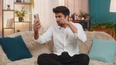 Evdeki koltukta oturan Hintli adam video görüşmesi sırasında tartışıyor, kulaklıkla konuşuyor. Arap adam hayal kırıklığına uğramış, duygusal, yükselen ses, stres, yoğun tepki, anlaşmazlık ve gerilimi ifade ediyor