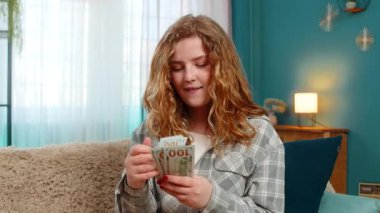 Genç bir kadın heyecanla elinde nakit dolarları sayıyor gülümsüyor ve beklenmedik mali kazancı kutluyor. Kanepedeki beyaz saçlı kız piyango kazanmasından, maaşından ya da sürpriz parasından memnun.