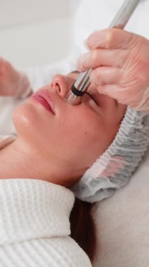 Enjeksiyonsuz mezoterapi ya da elektroporasyon. Güzellik doktoru, kadın müşteriyi güzellik kliniğinde terapiye götürür. Kız cilt bakımı anti-yaş spa prosedürü. Estetik kozmetoloji. Dikey video