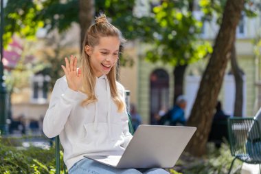 Park City caddesinde oturan genç bir kadın, dizüstü bilgisayara bakıyor, arkadaşlarıyla, ailesiyle ya da müşterisiyle görüntülü bir konferans görüşmesi yapıyor, uzak sohbetin tadını çıkarıyor. El sallayan genç kız