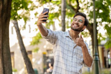 Neşeli Hintli blog yazarı akıllı telefondan selfie çekiyor, aile dostlarıyla internet üzerinden video görüşmesi yapıyor sosyal medya vlog 'u için hikayeler kaydediyor, el sallıyor. Şehir caddesindeki Arap adam..