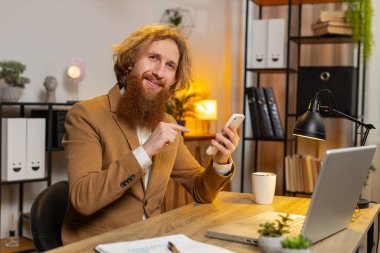 Kendine güvenen kızıl saçlı işadamı internet üzerinden akıllı telefon uygulaması kullanarak konuşuyor. Onaylıyor, uzaktan kumandayla çalışıyor. Kameraya bakan serbest çalışan bir adam. Reklamcılık