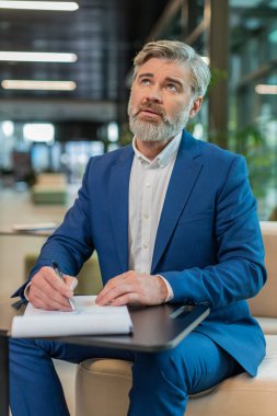 Beyaz tenli orta yaşlı işadamı belgelerle çalışıyor, bilgileri analiz ediyor, gazete okuyor mali rapor hazırlıyor. Takım elbiseli mutlu girişimci ofis lobisindeki grafik belgelerini inceliyor..