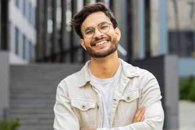 Mutlu Hintli genç bir adamın portresi güler yüzlü, kameraya bakan mutlu yüz hayal kuran, dinlenen rahatlayan, dışarıda iyi haberler veren. Şehirdeki Arap Hindu adam. İş adamları
