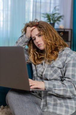 Evde dizüstü bilgisayarıyla oturan genç bir kadın başarısız bir denemeden sonra elini alnına koyduğu için hayal kırıklığına uğramış. Kanepede oturan beyaz saçlı kız, çözülmemiş internet sorununa duygusal tepki veriyor.