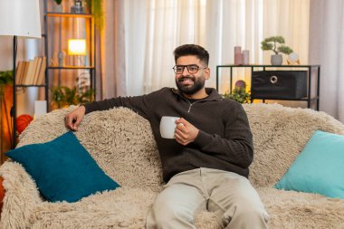 Evdeki Hintli adam kanepede oturur ve uzun bir günün ardından gülümseyen çay ya da kahvenin tadını çıkarır. Arap adam aroma soluyor ve huzurlu bir ruh hali ve huzur dolu bir an yaşıyor..