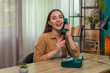 Masadaki genç kadın 90 'lardan kalma telefonları elinde tutuyor ve neşeli sohbetler sırasında yüksek sesle gülüyor. Kafkasyalı kız eğlenceli geçmişe dönük tarzdan hoşlanıyor ve neşeli konuşmalar yaparak parlak enerjisini ifade ediyor.