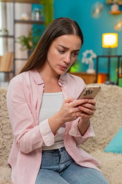 Genç bir kadın evdeki kanepede oturmuş akıllı telefon konuşmaları yapıyor ve olumsuz mesajlara sinirle el sallıyor. Kafkasyalı kız, internet üzerinden kelimelere tepki gösteren hoşnutsuz görünüm ve duruş gösteriyor..