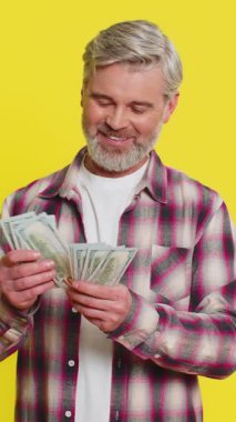 Olgun bir adam, maaş tasarruflarından duyulan memnuniyeti yansıtan dolar banknotlarını dikkatle sayar. Sarı arka planda orta yaşlı bir adam kazançlı bir ödülden gurur duyuyor.