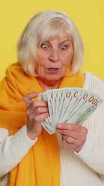 Zengin, mutlu, yaşlı bir kadın hayran, başarılı iş kariyeri, piyango talihlisi, yüksek gelirli emeklilik maaşı gibi banknotlar sallıyor. Sarı arka planda yaşlı bir büyükanne.
