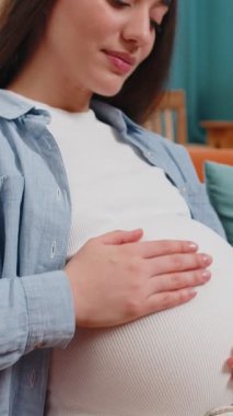 Evdeki rahat koltukta oturan, göbeğini okşayan, rüya gören, mutlu, hamile bir kadın. Hamilelik sırasında gülümseyen, beyaz, müstakbel kadın anne bebek bekliyor..