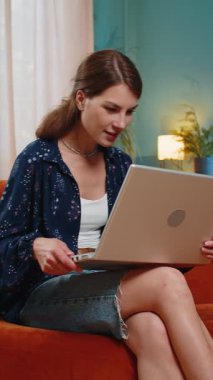 Laptop kullanan Kafkasyalı genç kadın, iyi haberler aldı. Aniden kazanılan zaferle şok oldu. Dairede piyango ikramiyesini kutladı. Neşeli kız evdeki salonda kanepede çığlık atıp dans ediyor.