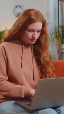 Evdeki kanepede oturan genç ve üzgün beyaz kadın dizüstü bilgisayar kullanıyor ve stres altında. Kaybına tepki veren kızıl saçlı kız. Oturma odasındaki internet sitesinde kötü haber. Bilgisayar virüsü.