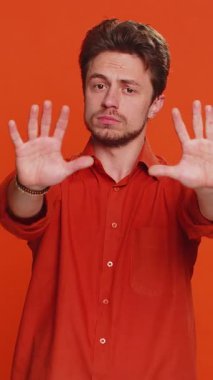 Dur, yeter. Beyaz adam, hiçbir avuçiçi kapalı el hareketinin bitiş işareti, bitiş uyarısı, erişime izin verilmemesi, iletişimin azalması, vücut dili tehlikesi olmadığını söylüyor. Turuncu arka plandaki genç adam.