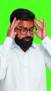 Hintli adam kafaya eliyle dokunur ve gergin görünür. Duygusal baskı, acı ya da iç stres gösterir. Yeşil krom anahtar arka planda izole edilmiş bir Arap adam endişe ve zihinsel rahatsızlık reaksiyonu gösteriyor