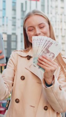 Akıllı telefon kullanan ve Ukrayna Hrivnias UAH nakit paralarını elinde tutan mutlu ve olgun bir iş kadını şehir merkezinde duruyor. Başarılı iş kariyeri, piyango kazananı, büyük gelir, zenginlik