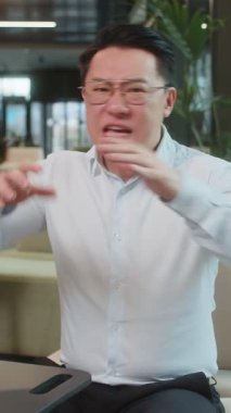 Tişörtlü kızgın yetişkin patron ofisteki modern işyerindeki kameraya bakarak video konuşması yapıyor. Tatminsiz Çinli iş adamı, şirket sorunları hakkında astlarıyla iletişim kuruyor..