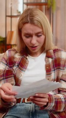 Genç yetişkin bir kadın, yüksek masrafları gözden geçirdikten sonra elinde faturalarla hayal kırıklığı içinde başını sallıyor. Sarışın kız hayal kırıklığıyla tepki veriyor. Finansal baskı ve artan maliyetler konusunda endişeli.