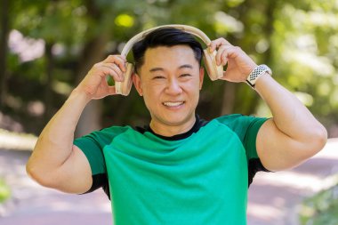 Mutlu genç Japon adam kablosuz modern kulaklık taktı. Koşu koşucusu, spor koşucusu, parkta koşan, müzik dinleyen, müzik dinleyen, koşan, sağlıklı bir yaşam tarzı olan erkek..