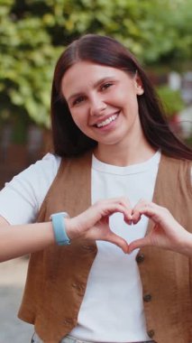 Ben de seni seviyorum. Beyaz kadın aşkın sembolünü yapar, kameraya kalp işaretini gösterir, romantik duyguları ifade eder samimi olumlu duyguları ifade eder. Sadaka, minnettarlık, bağış. Şehir caddesinde açık hava