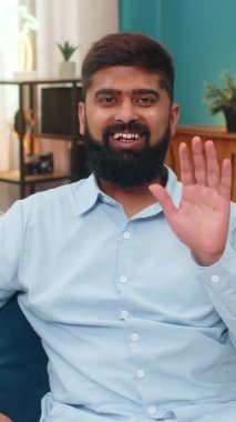 Kameraya el sallayan Hintli adam akıllı telefon görüntülü sohbet programında dostça gülümsüyor. Kanepedeki Arap adam izleyicileri selamlıyor. Neşeli jest, sıcak karşılama, olumlu ruh hali, uzaktan iletişim..