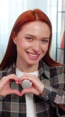 Evdeki genç kadın sevgi ve şefkat göstermek için parmaklarıyla kalp şeklinde gülümsüyor. Kanepede oturan beyaz saçlı kız olumlu duygular, ilgi ve jestle tatlı bir bağ kuruyor.