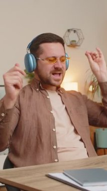 Evde dizüstü bilgisayarı olan, kulaklık takan ve güneş gözlüğü takan neşeli, rahat genç iş adamı favori disko müziğini dinliyor, dans ediyor. Serbest çalışan adam dinleniyor, mola veriyor, kutluyor..