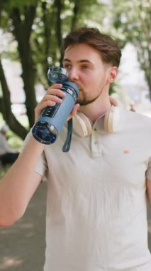 Sportif atletik susamış beyaz erkek koşucu parkta çalıştıktan sonra su içiyor, spor şişesi içiyor aktif genç yaşam tarzı ferahlatıcı su içiyor gülümseyerek uzaklaşıyor..