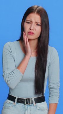 Diş sorunları. Yanağa dokunan genç bir kadın, korkunç bir ifadeyle gözlerini kapatan diş ağrısı, hassas dişler, çürükler. Güzel esmer kız mavi stüdyo arka planında izole edilmiş.