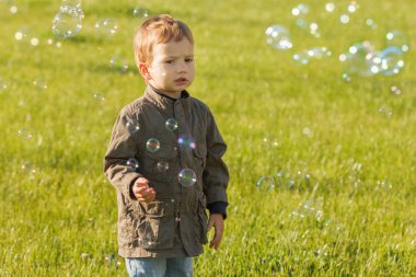Sabun köpüğü üfleme yaz parkta küçük bir çocuk. Çim açık arka plan.