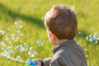 Sabun köpüğü üfleme yaz parkta küçük bir çocuk. Çim açık arka plan.