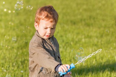 Sabun köpüğü üfleme yaz parkta küçük bir çocuk. Çim açık arka plan.