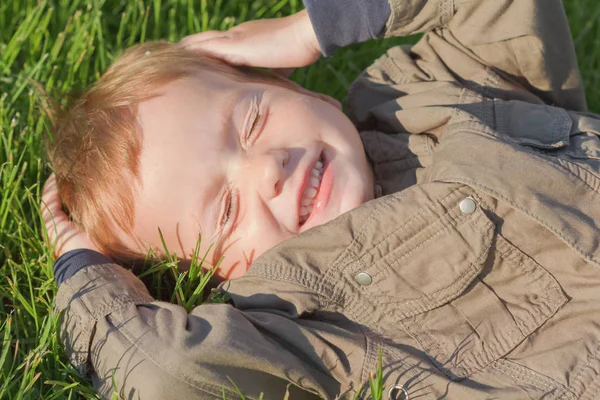 Gelukkig, glimlachen jongen opleggen van een gras in een park — Stockfoto