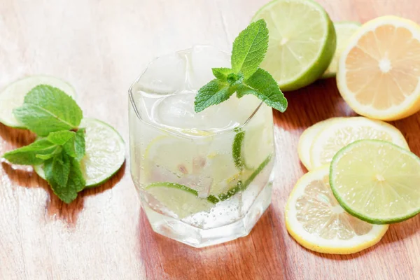 Un vaso de agua fría con limón y lima, cubitos de hielo y hojas de menta — Foto de Stock