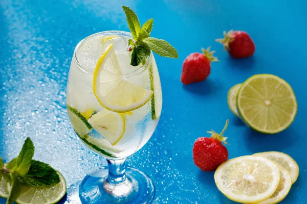 Mojito-Cocktail mit Limette und Minze im Glas auf nassem Glastisch mit blauem Hintergrund — Stockfoto