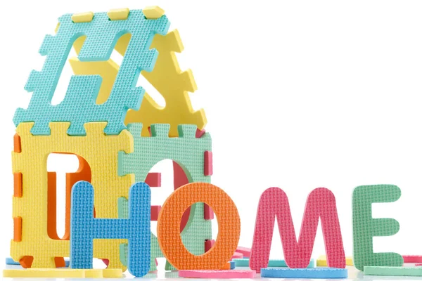 La colorida palabra "HOME" junto a una pila de otras letras sobre la composición de la superficie de la pizarra blanca — Foto de Stock