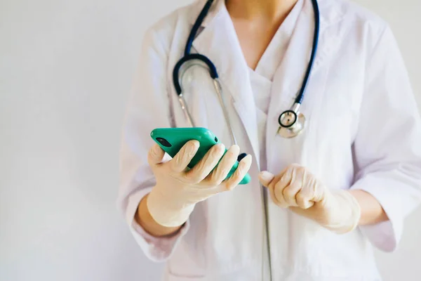The girl doctor is holding a smartphone. The doctor\'s hands are wearing rubber gloves. The doctor corresponds on social networks.