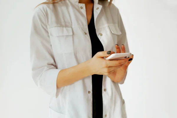 Girl doctor with smartphone in hand. A doctor in a white coat with a smartphone in his hands with black manicure. Close-up in the hands of a mobile phone. Black manicure. Pink case.