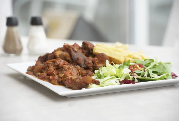 Cooked rabbit served with fresh vegetables and potatoes on a white plate with blurry background. Delicious maltese rabbit served in the restaurant. Maltese food. Malta cuisine