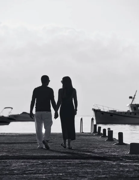 Couple walking near the sea in B&W photo, man and woman going to harbour in Malta, man and woman walking with fishing ships background, conceptual photo of bright future
