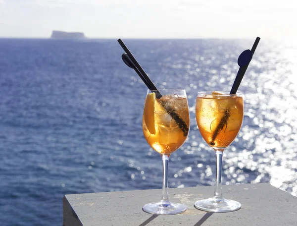 Two glasses of  Cocktail isolated in sea background with the view to little maltese island Fifla. Summer drink