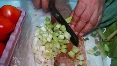 Mutfaktaki ahşap kesme tahtasının üzerinde taze yeşil soğan doğruyorum.